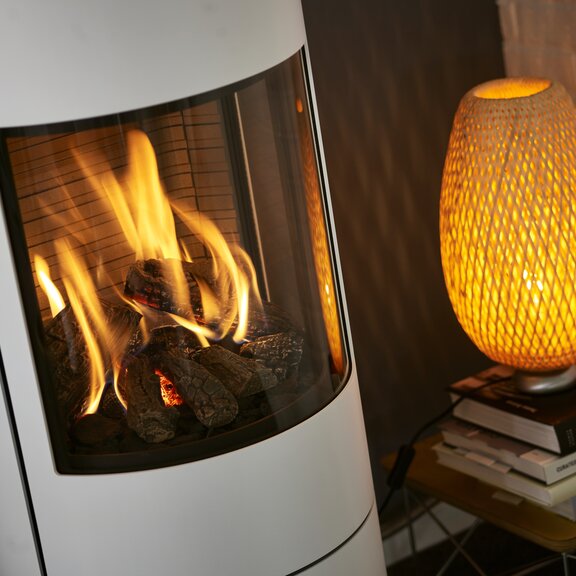 Feuerraum vom Gas-Kaminofen VIVA L in Weiss mit Stahltür und Seitenfenster und angenehm brennender Gasflamme